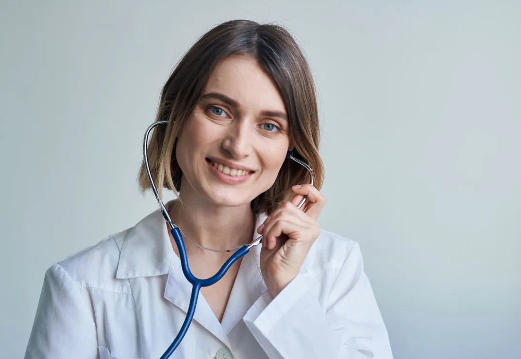 Uma médica sorri enquanto segura um estetoscópio em volta do pescoço.